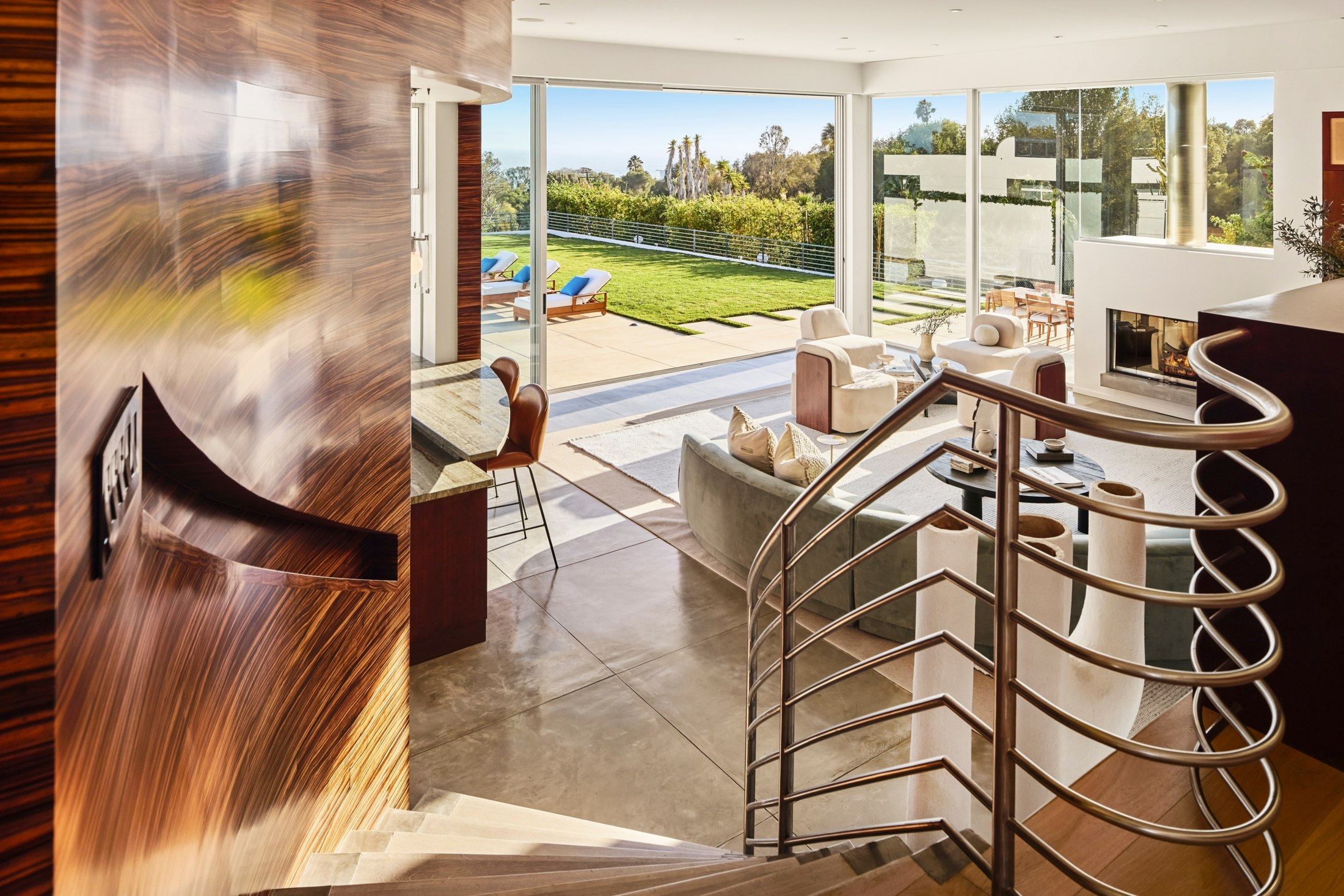 Looking outward through the great room’s open glass walls toward the lawn, palms, and ocean beyond